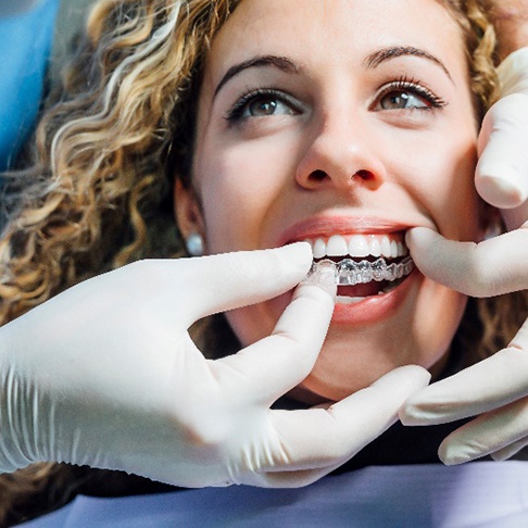 Patient smiling while dentist places Invisalign aligner on top teeth