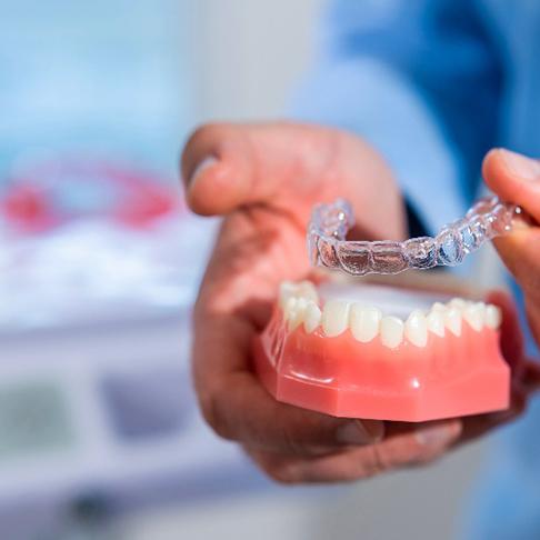 Dentist placing Invisalign aligner over model of teeth