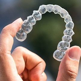 Patient holding up Invisalign clear aligner outside