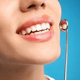 A closeup of a young woman using a dental mirror on her teeth